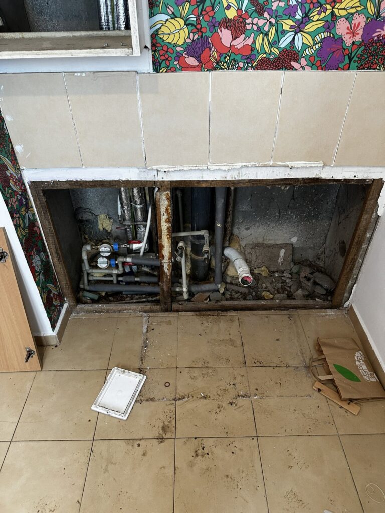 Remont wnętrza z widocznymi instalacjami w trakcie wykończenia. Prace realizowane przez firmę remontową, które obejmują wymianę rur oraz przygotowanie podłogi do dalszych prac.