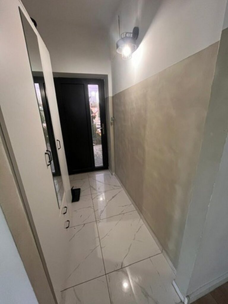 Wnętrze przedpokoju po remoncie, z nowoczesnymi wykończeniami, podłogą z płytek ceramicznych i funkcjonalną szafą. Idealne rozwiązanie dla osób szukających inspiracji do remontu i wykończenia wnętrz.