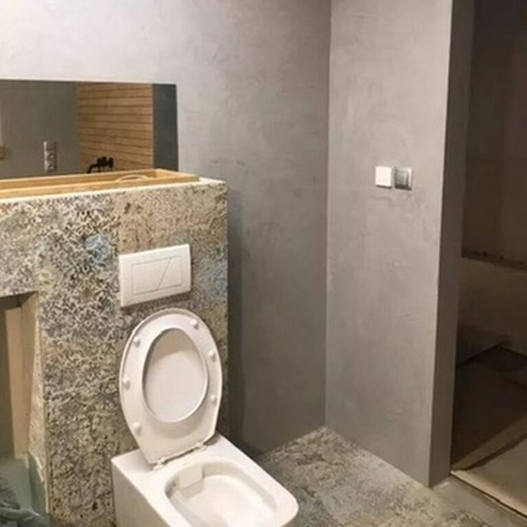 Nowoczesna łazienka po remoncie, z eleganckimi wykończeniami wnętrz i minimalistycznym designem. Widać strefę z toaletą oraz elementy szaro-beżowego tynku. Idealny przykład pracy profesjonalnej firmy remontowej.