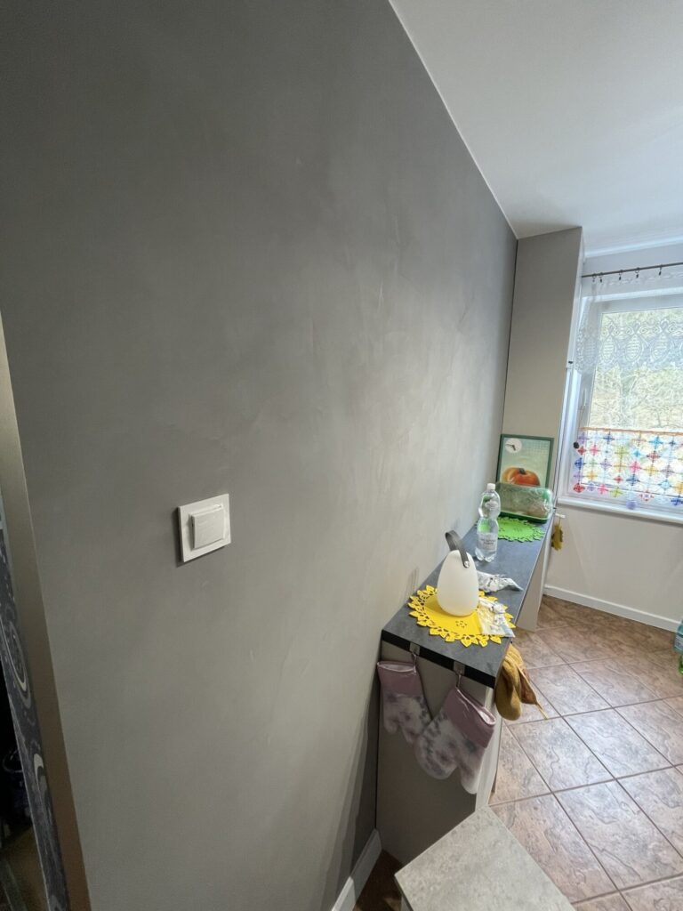 Remont ściany w kolorze szarym w nowoczesnym wnętrzu, wykonany przez firmę remontową. Wykończenia wnętrz podkreślają elegancki styl pomieszczenia.