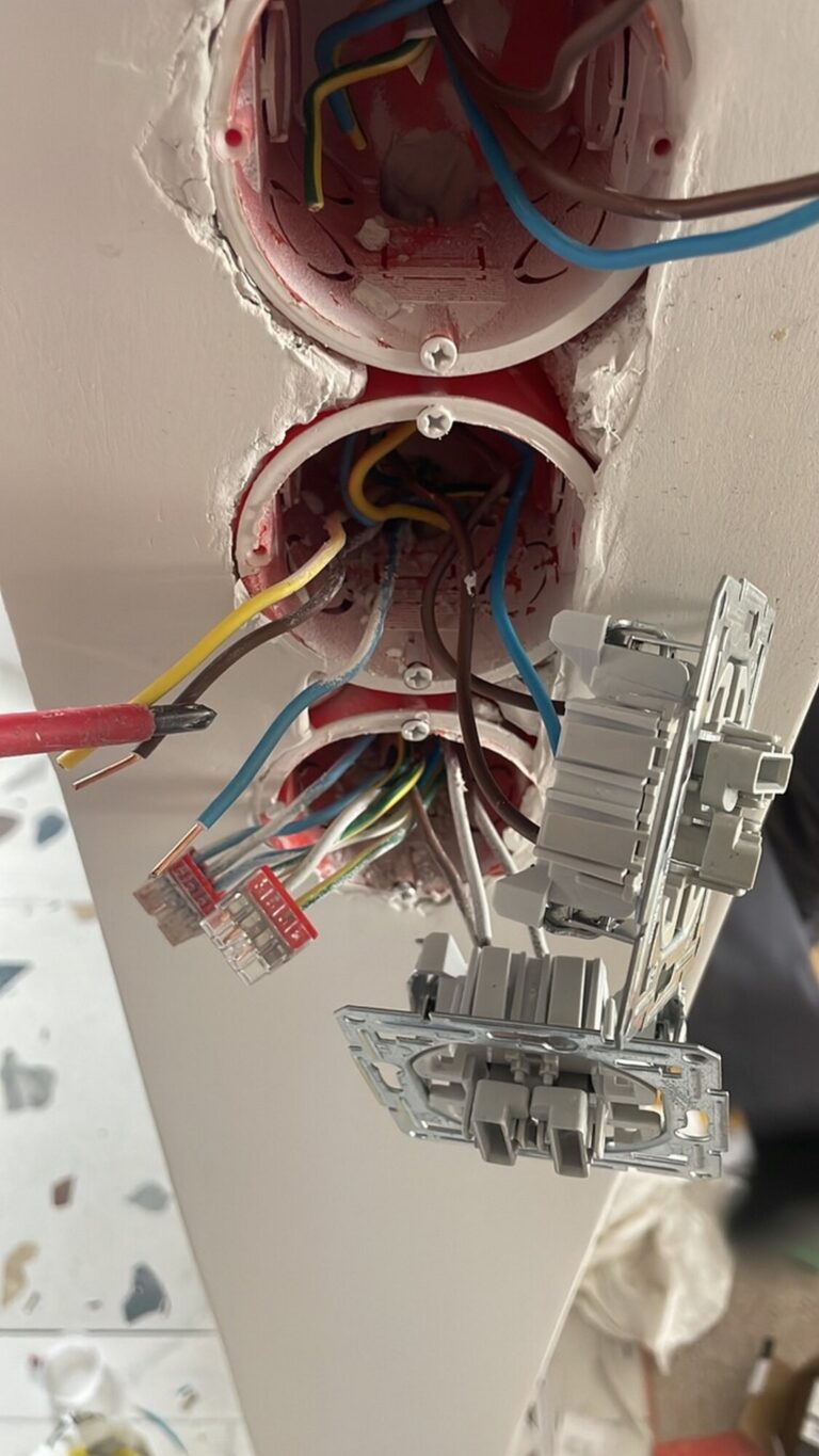 Widok instalacji elektrycznej z zamontowanymi gniazdkami, elementami przewodów oraz narzędziami remontowymi, idealny do dokumentacji działań firmy remontowej zajmującej się wykończeniem wnętrz.