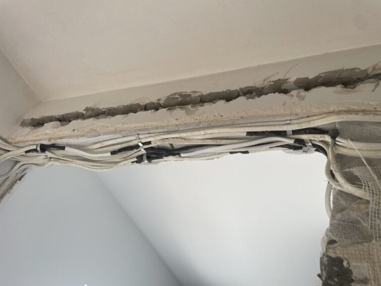 Prace remontowe z widocznymi instalacjami elektrycznymi i uzupełnieniem tynku w trakcie wykończenia wnętrz. Fachowa firma remontowa oferująca kompleksowe usługi.