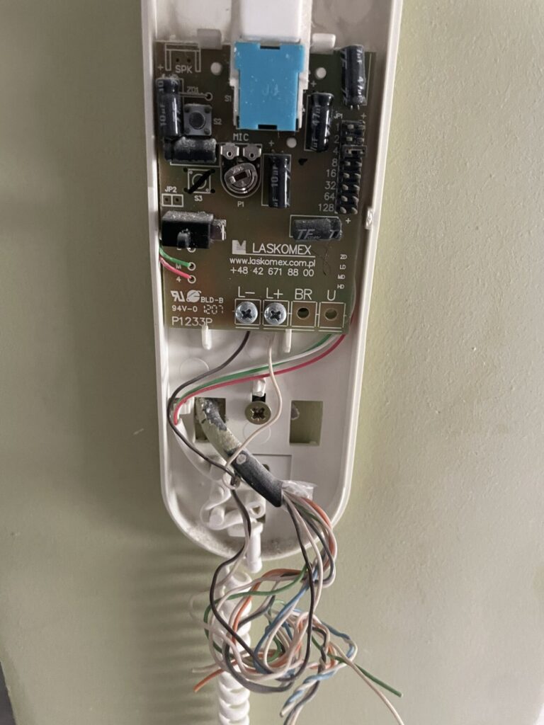 Zbliżenie na uszkodzony panel elektryczny w trakcie remontu, pokazujący kable i komponenty. Idealne dla firmy remontowej zajmującej się wykończeniami wnętrz.