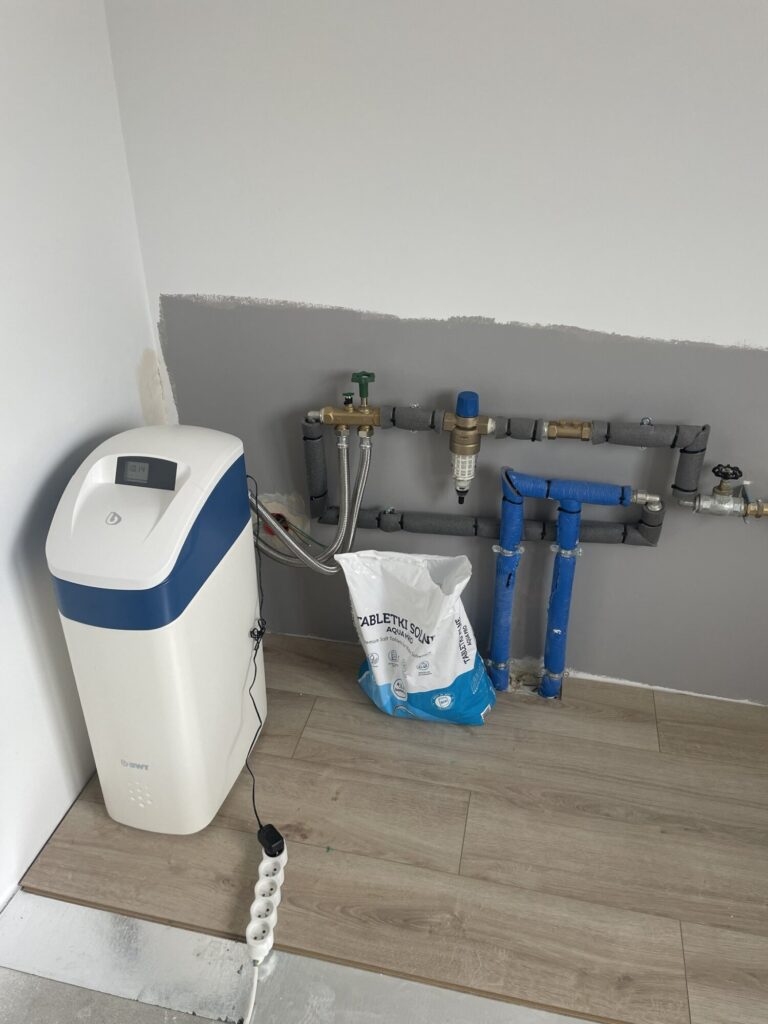 Instalacja hydrauliczna w trakcie remontu wnętrza, z widocznym urządzeniem do uzdatniania wody. Profesjonalne wykończenie wnętrz przez firmę remontową.