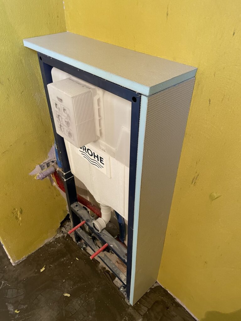 Zainstalowana uniwersalna stelażowa konstrukcja do WC, będąca częścią remontu wykończeń wnętrz, w nowoczesnej łazience. Firma remontowa przygotowuje przestrzeń pod dalsze prace.