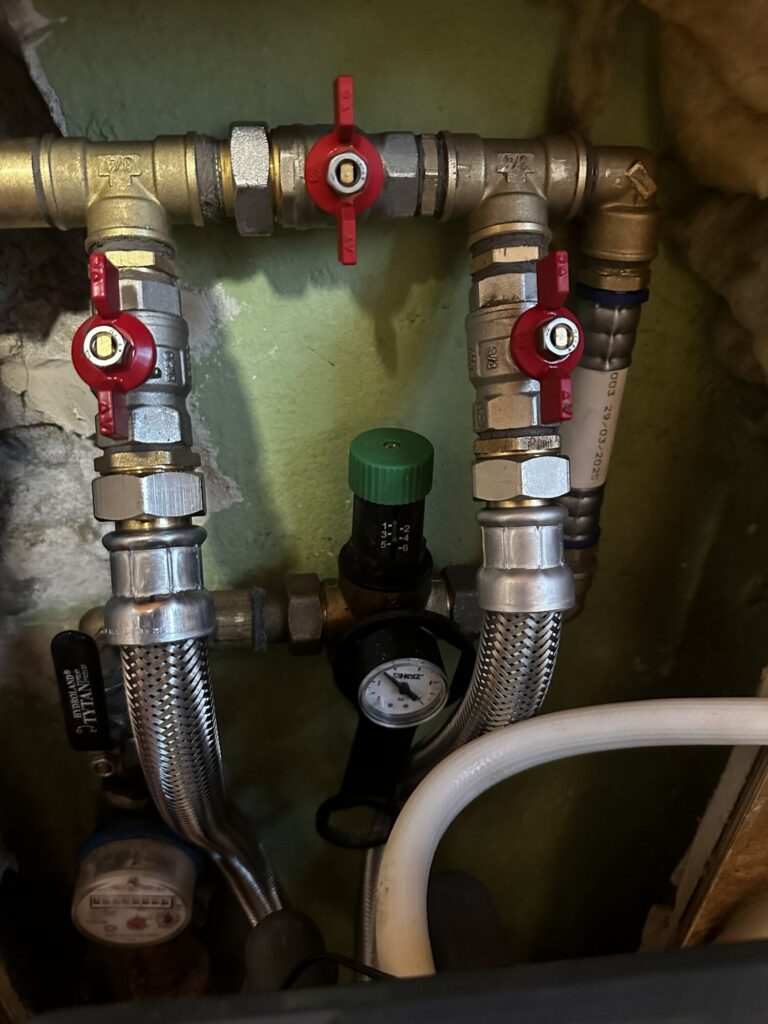 Zestaw nowoczesnych zaworów i manometr w instalacji hydraulicznej, używany w remontach i wykończeniach wnętrz. Firma remontowa oferująca usługi związane z modernizacją systemów wodno-kanalizacyjnych.