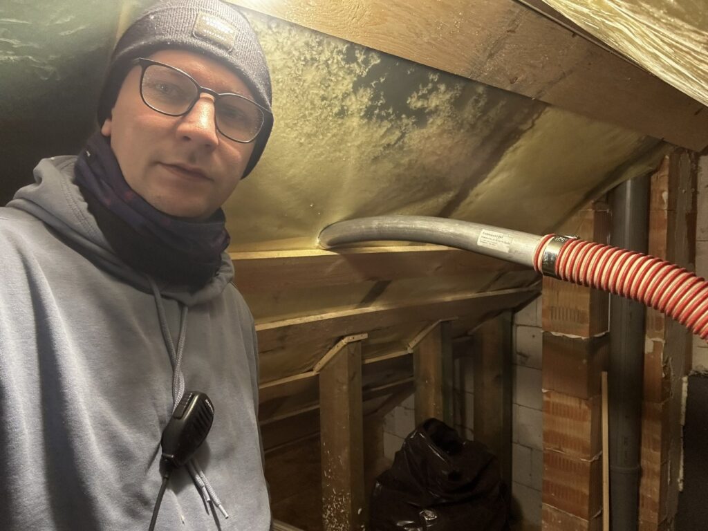 Przywidz - Mężczyzna podczas remontu poddasza, z narzędziem w ręku, przygotowujący wykończenia wnętrz. Fachowiec z firmy remontowej pracuje nad izolacją, zapewniając profesjonalną obsługę.
