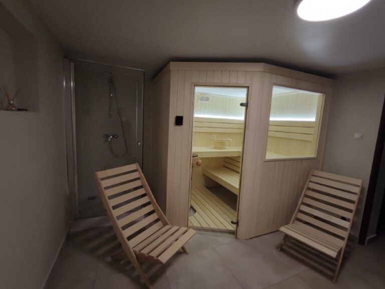 Nowoczesna sauna w pomieszczeniu po remoncie, z drewnianym wykończeniem, idealna do relaksu. W tle prysznic, co podkreśla funkcjonalność wnętrza. Firma remontowa zapewniła estetyczne oraz praktyczne wykończenia, tworząc przytulne miejsce do wypoczynku.