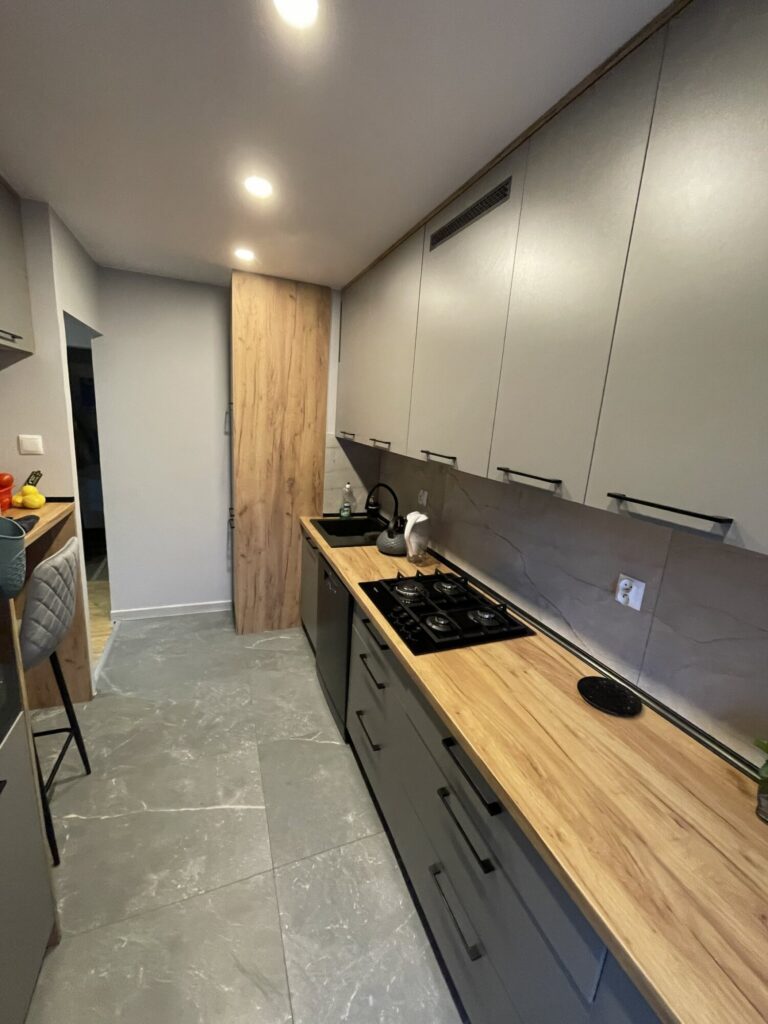 Nowoczesna kuchnia po remoncie z eleganckimi wykończeniami wnętrz. Szare meble kuchenne i drewniane blaty podkreślają styl aranżacji. Idealna dla osób szukających inspiracji do remontu.