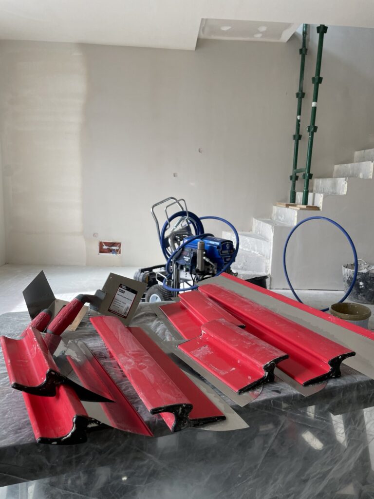Wnętrze w trakcie remontu z narzędziami do wykończenia, w tym elementy do gładzi. Firma remontowa przygotowuje przestrzeń do dalszych prac wykończeniowych.