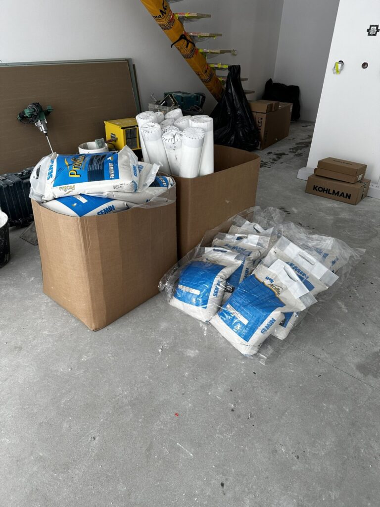 Wnętrze w trakcie remontu z kartonami materiałów budowlanych i workami z wykończeniami. Prace prowadzi firma remontowa, która dostarcza niezbędne akcesoria do wykończeń wnętrz.