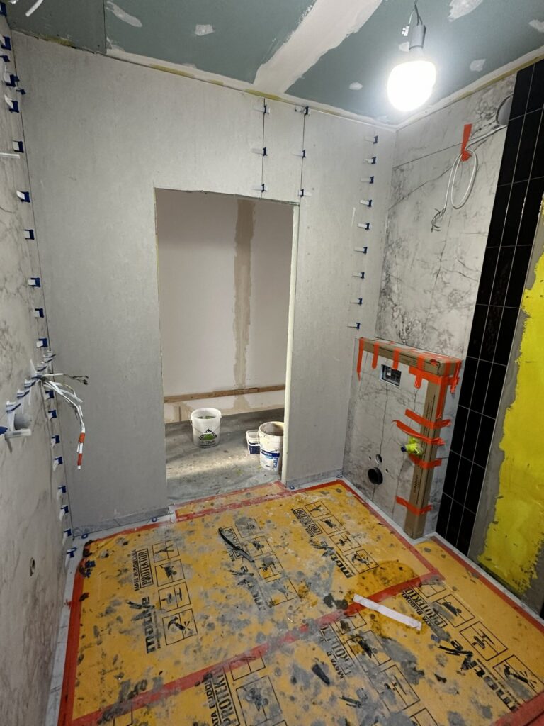 Remont wnętrza łazienki w trakcie prac wykończeniowych, widoczne przygotowania do położenia płytek. Elementy elektryczne oraz materiały budowlane w tle. Idealne rozwiązanie dla klientów poszukujących profesjonalnej firmy remontowej.