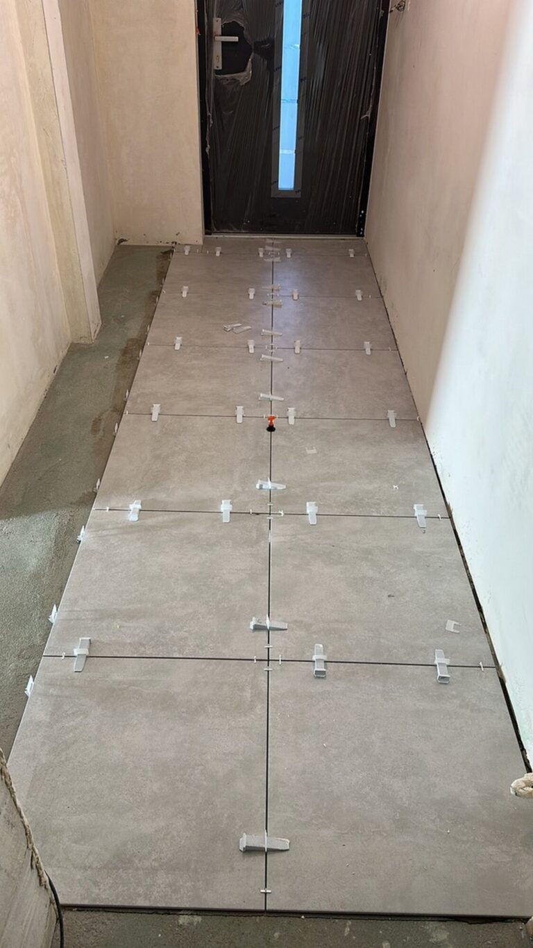 Nowe płytki ceramiczne układane w korytarzu w trakcie remontu przez firmę remontową, z widocznymi spacjami na fugowanie oraz zabezpieczeniem powierzchni.