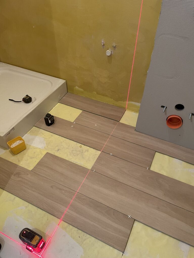 Remont łazienki z zastosowaniem laserowego wytyczania podłogi. Widok na układanie podłogi z paneli w nowoczesnym wnętrzu. Firma remontowa przygotowuje wykończenia wnętrz w wysokiej jakości.