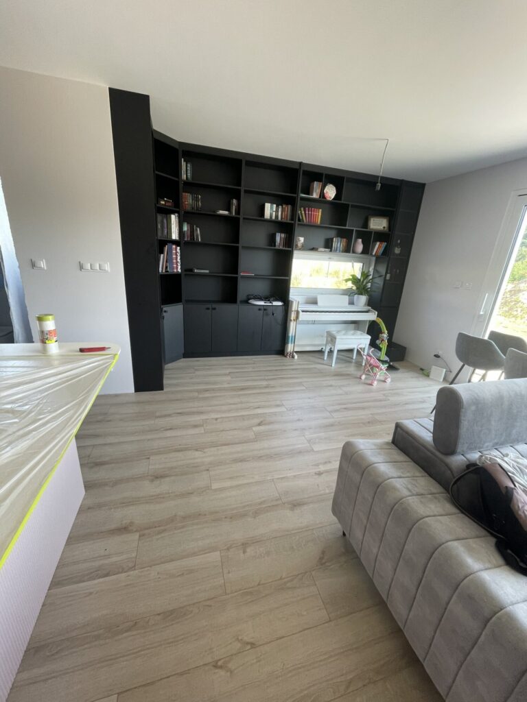 Kartuzy - Nowoczesny salon po remoncie z szarym narożnikiem i czarną biblioteczką. Idealne wykończenia wnętrz, kt&oacute;re podkreślają elegancję przestrzeni. Usługi firmy remontowej zapewniają wysoką jakość wykonania.
