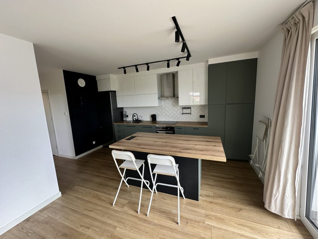 Kartuzy - Elegancka kuchnia po remoncie z nowoczesnymi wykończeniami wnętrz, idealna do inspiracji dla os&oacute;b szukających usług firmy remontowej. Szklane płytki, drewniany st&oacute;ł i minimalistyczne meble tworzą funkcjonalną przestrzeń.