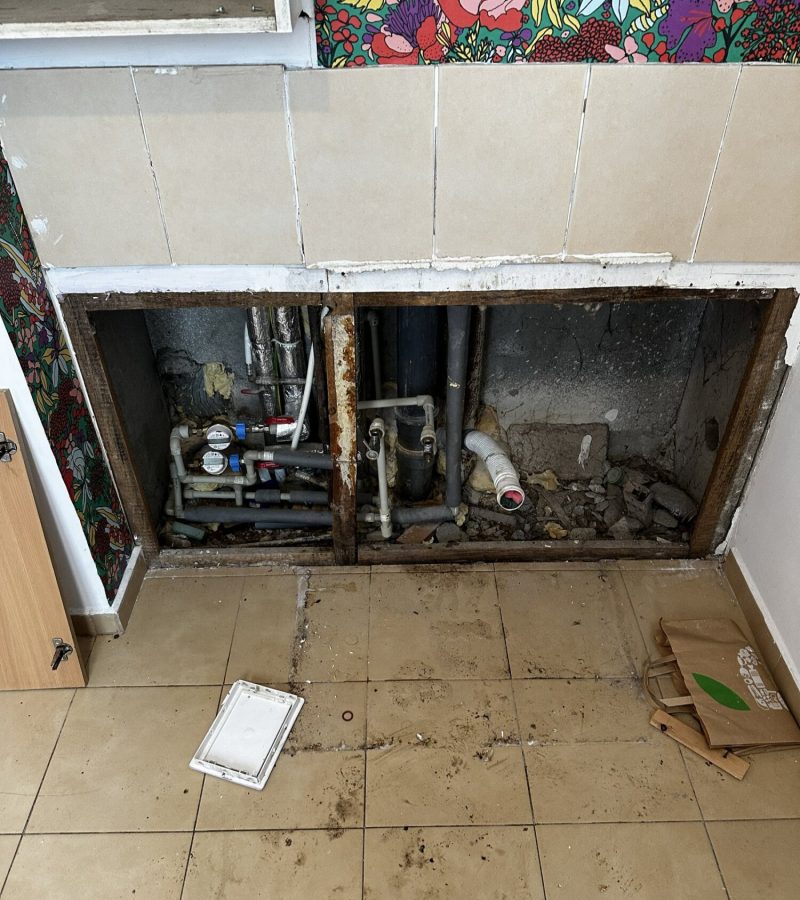 Remont wnętrza z widocznymi instalacjami w trakcie wykończenia. Prace realizowane przez firmę remontową, które obejmują wymianę rur oraz przygotowanie podłogi do dalszych prac.